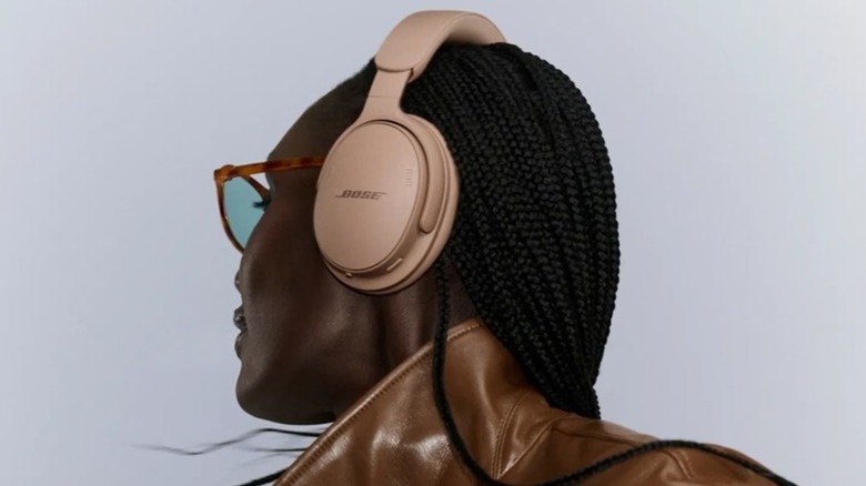 A closeup of an individual with turtle-shell glasses and a brown leather jacket wearing a pair of second-generation Bose QuietComfort Headphones in Hazelnut Taupe
