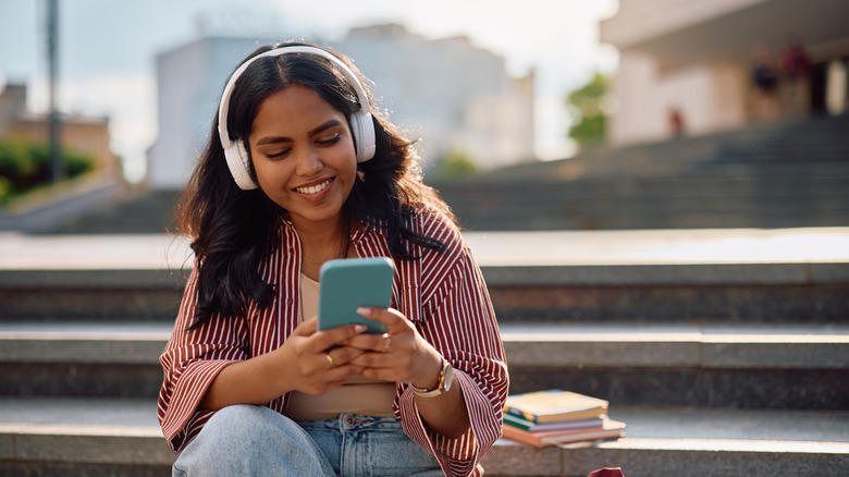 A woman using over-ear headphones in an outdoor setting.