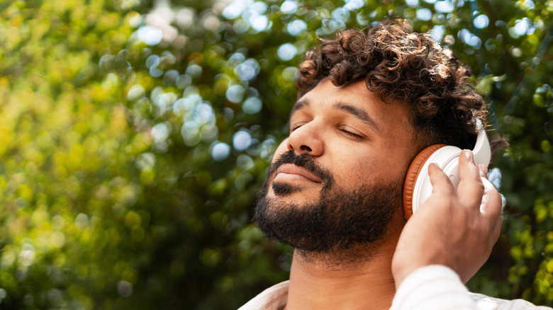 A bearded man wears a pair of white and orange headphones in an outdoor setting.