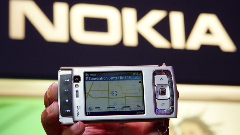 Nokia N95 held in hand showing screen, with nokia logo behind