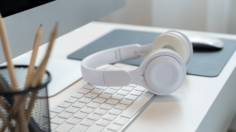 A pair of Bluetooth headphones on a computer desk.