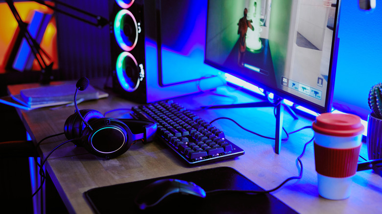RGB-lit gaming desk with monitor, keyboard, headset, mouse pad, and a PC tower in the background