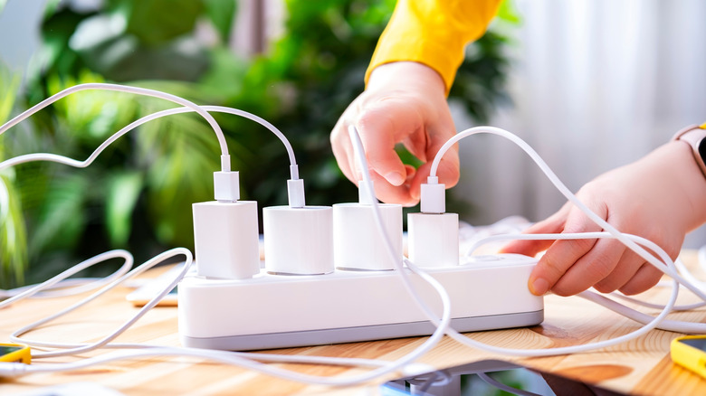 person reaching for one of several phone chargers plugged into a surge protector