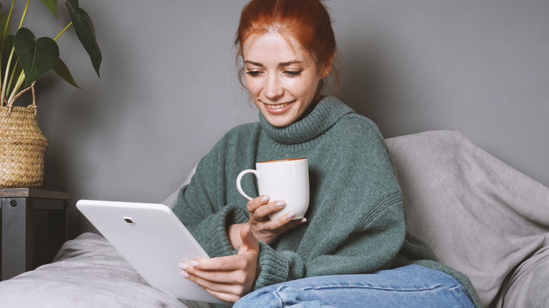 Woman holding tablet and coffee mug on cozy seat