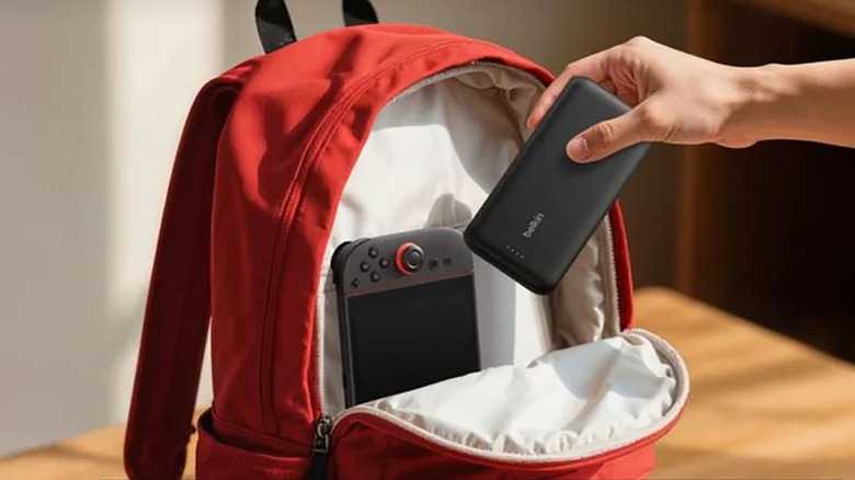 A hand putting a Belkin charger into a red backpack with the Nintendo Switch 2.