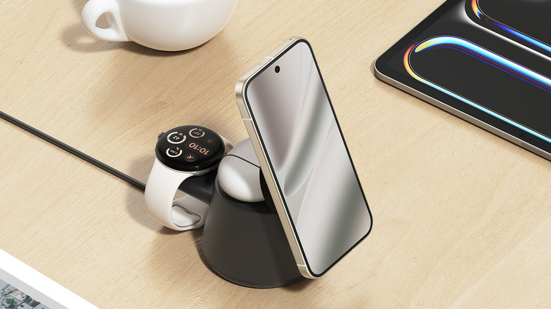 A phone, Pixel Watch, and Google Pixel buds mounted on a Belkin modular charging dock with a tablet and coffee mug on the table beside it.