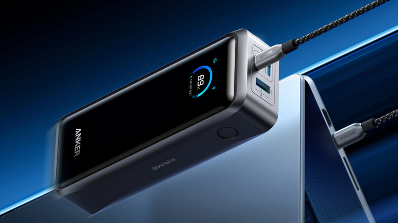 Close-up of a black Anker power bank with a battery life display on the front and a USB-C cord plugged into the battery and a laptop
