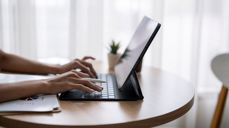 A woman seen typing on a tablet keyboard with a pen in her hand.