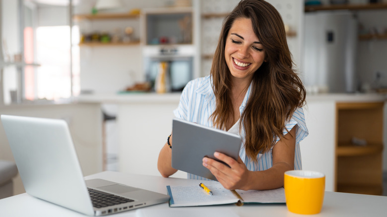 Person smiling while using a tablet beside a laptop.