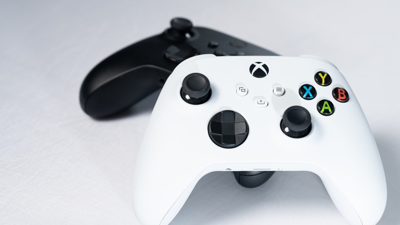 two xbox controllers laying on a white background, white and black controller leaning against each other