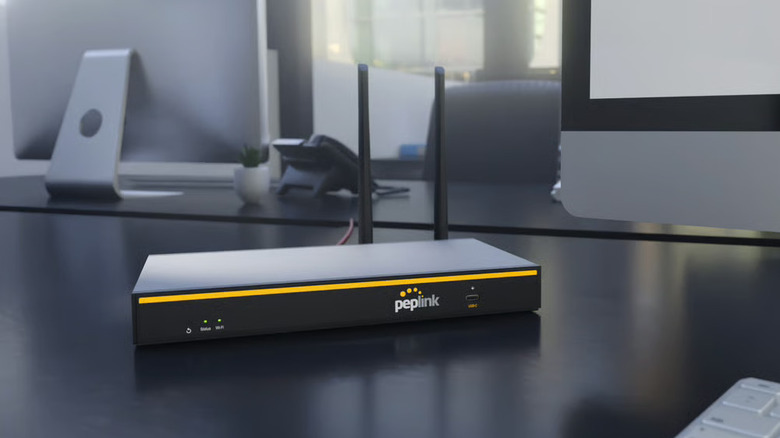 The Peplink B One router on a desk next to a computer