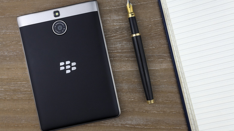 A BlackBerry Passport face down on a table beside a pen and notepad.