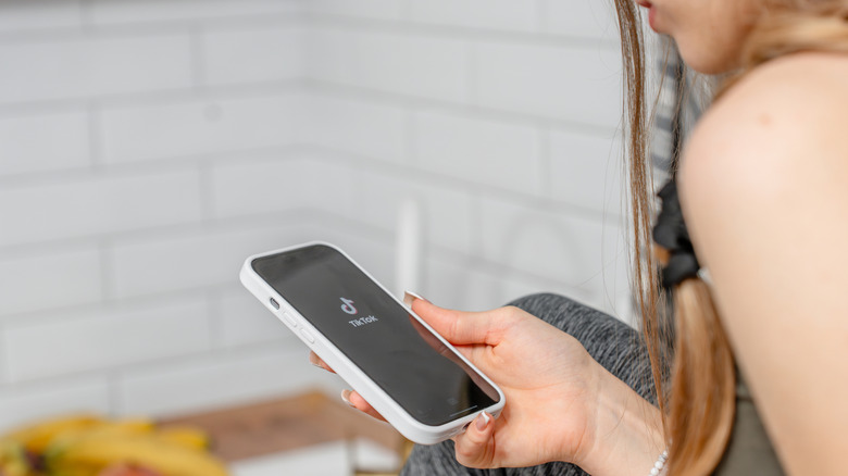 A young person opening the TikTok app on her smartphone.