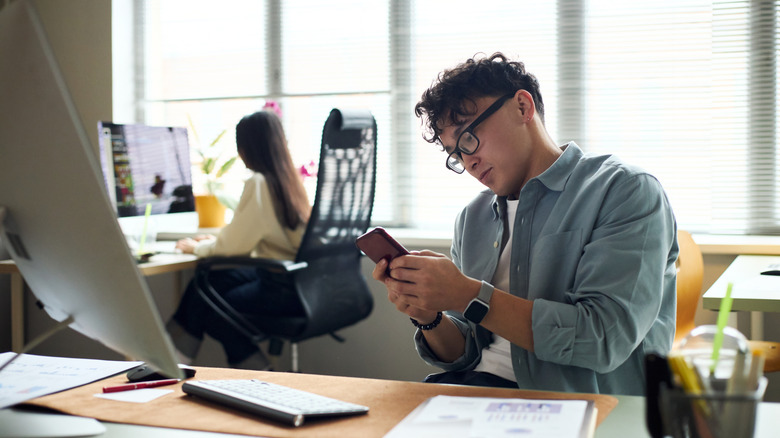 A young person at work using a smartphone.