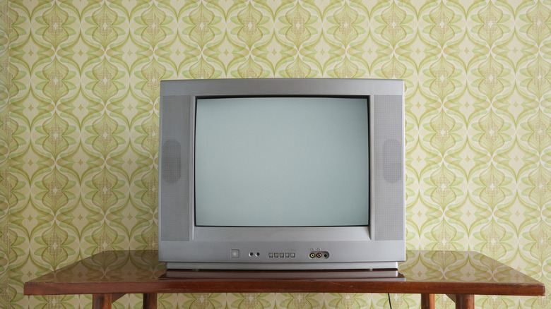 Old TV on the nightstand against the background of wallpaper.