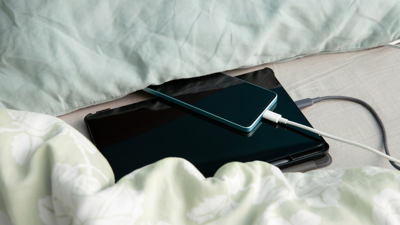 Phone and tablet charging on bed near pillows and blanket