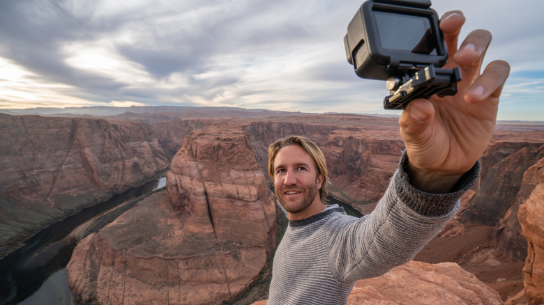 View of a man taking selfie picture with a GoPro action camera at the famous horseshoe bend by the Colorado river at sunset, beautiful dramatic colourful sky. people travel concept