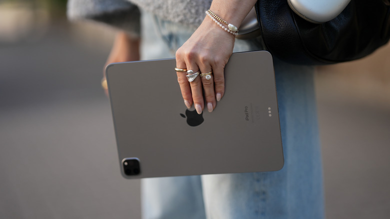 A model carries an iPad in her left hand as she stands in a city square