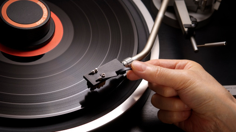 Turntable with Audio-Technica record weight on record, with hand moving needle to play
