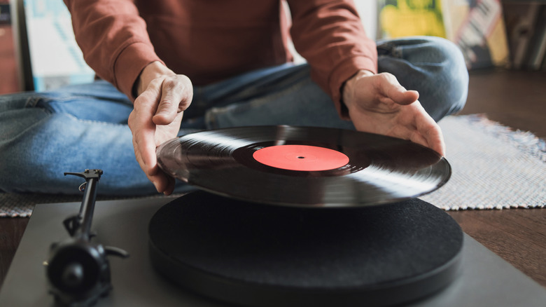 Person placing vinyl record on turntable sitting on floor cross-legged