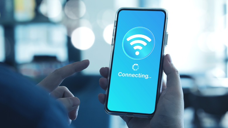 Smartphone in hand with display showing connecting and Wi-Fi signal.
