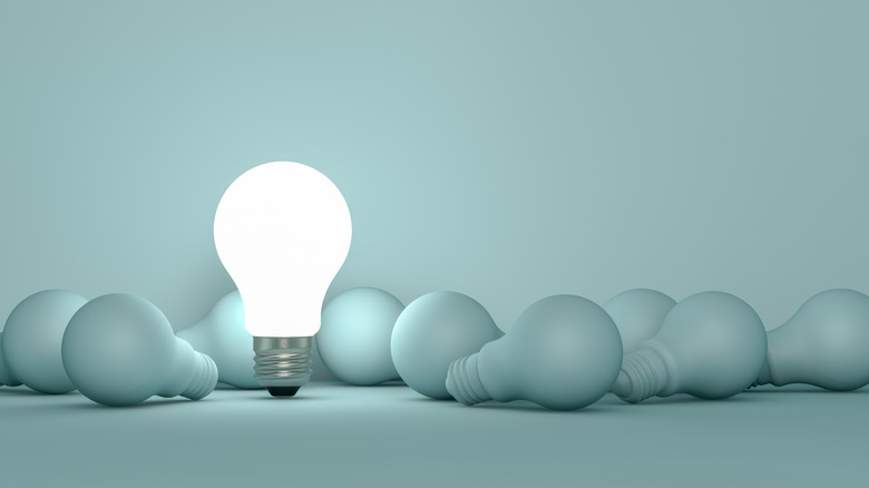 Several loose light bulbs lying on a blank background with one upright glowing one on the center lefthand side