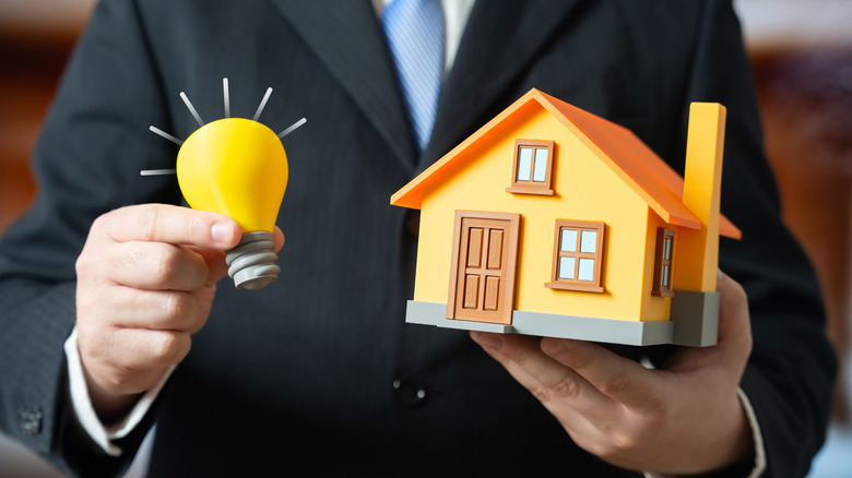 A man in a suit holding up a light bulb and a model of a house