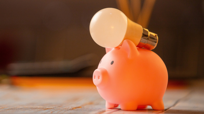 A light bulb lying on top of a small piggy bank