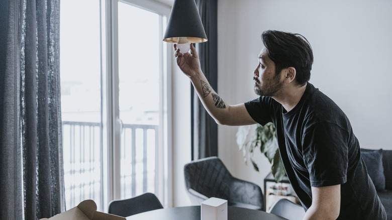 A man screwing a light bulb into a gray fixture coming from the ceiling