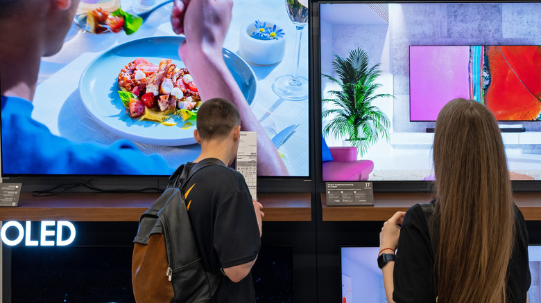 Shoppers looking at a display wall of Samsung OLED TVs.