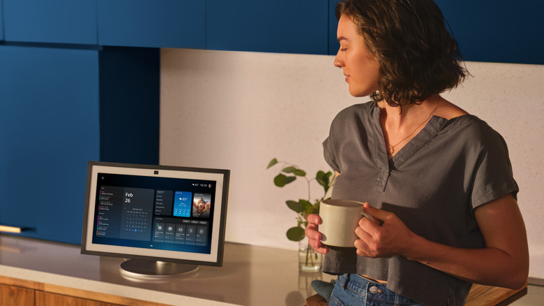 A woman stands with a coffee cup in her hands next to an Alexa+ enabled Echo