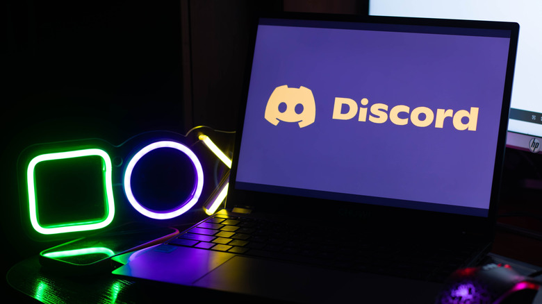 Discord logo on a laptop next to lit up gaming button symbol decorations in a darkened room