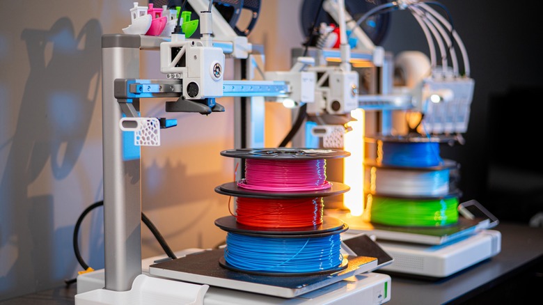 Two 3D printers side by side with several spools of filament atop each