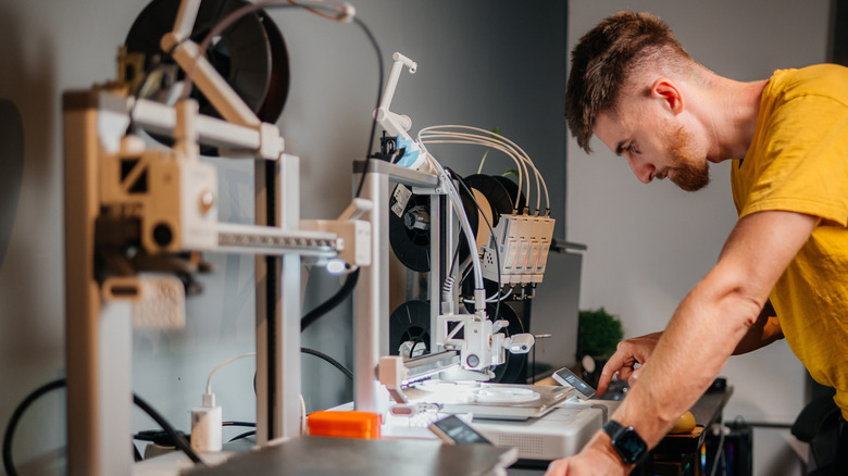 Person leaning against desk and interacting with a 3D printer