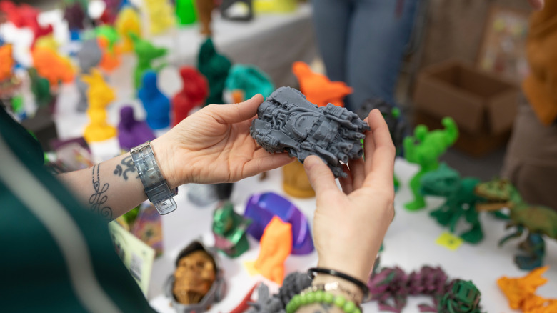 Person holding 3D printed vehicle in front of a table of 3D printed goods
