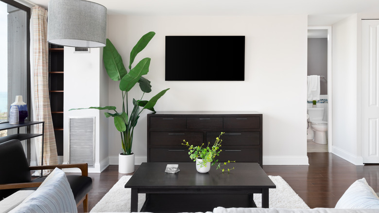 A minimalist living room with a wall-mounted flat-screen TV above a dark wood dresser.