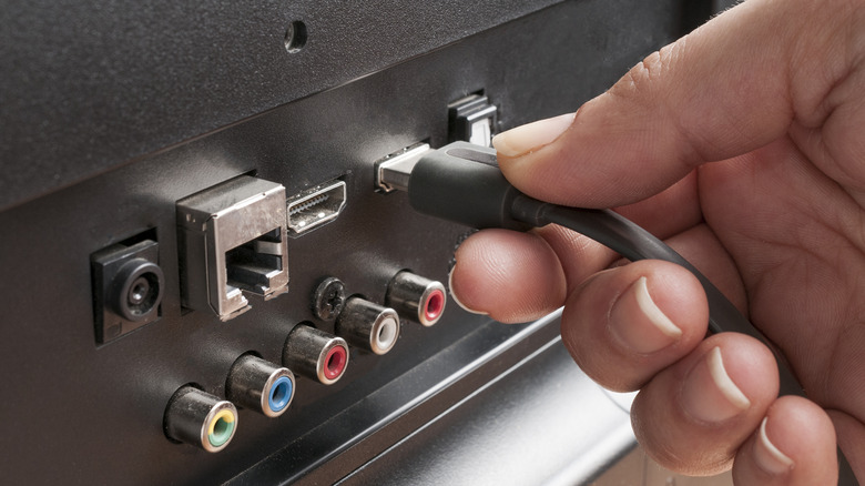 A close-up of a hand plugging an HDMI cable into the back of a television.