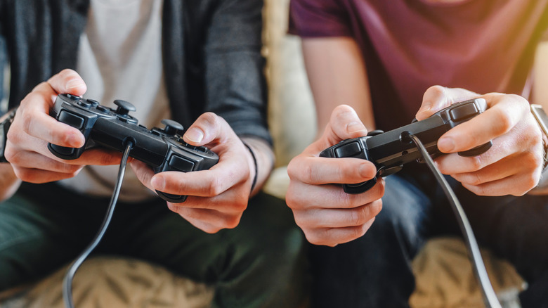 Two people playing a video game with wired controllers.