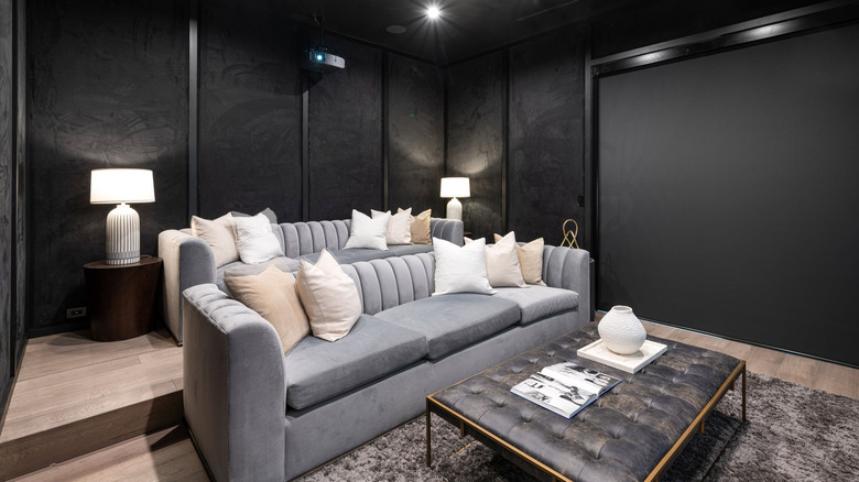 A dedicated home theater room with a projector, screen, and large sectional sofa.