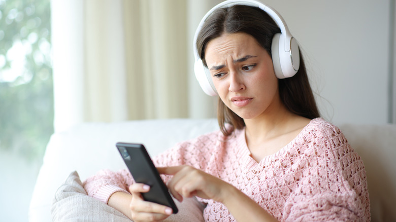 Person looking confused and disgusted while checking phone and wearing headphones