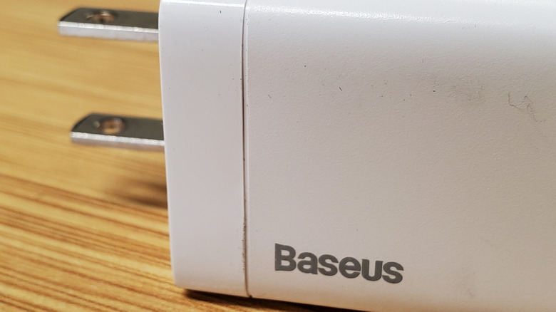 Baseus logo on a white cellphone charger on a light wooden surface