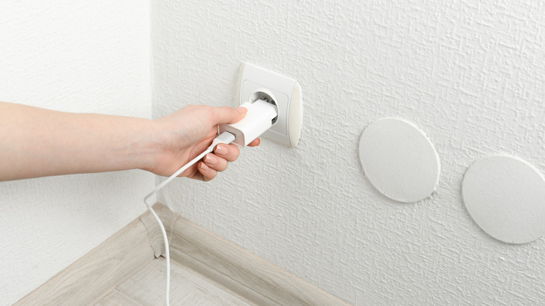 A person plugging a USB power adapter with charge cable into an electrical socket