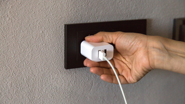 A person plugging a white USB charger into a black wall socket