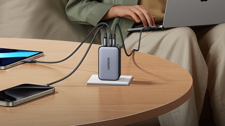 A Ugreen charger attached to a power socket on a wooden table with multiple devices charging