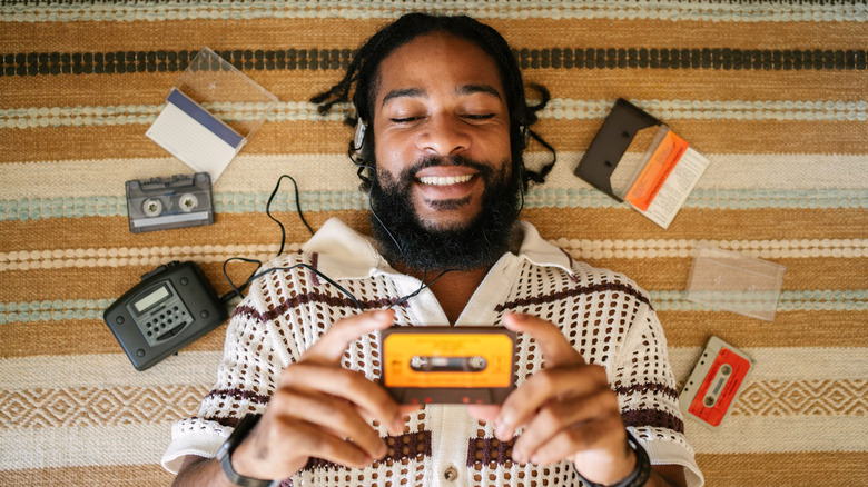 A man listening to music on a cassette player with other cassettes around him on the floor