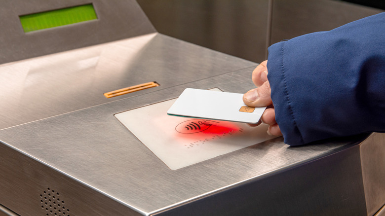 A person tapping an NFC-compatible card on a tap sensor at a transit gate