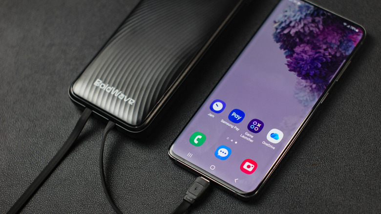 A phone connected to a portable power bank on a black background.