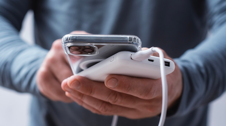 A man's hands holding a power bank and a phone.