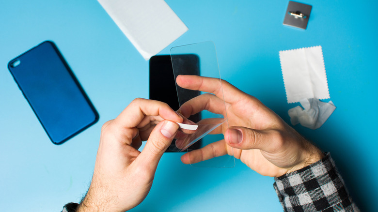 A person applying a tempered glass screen protector to a smartphone screen