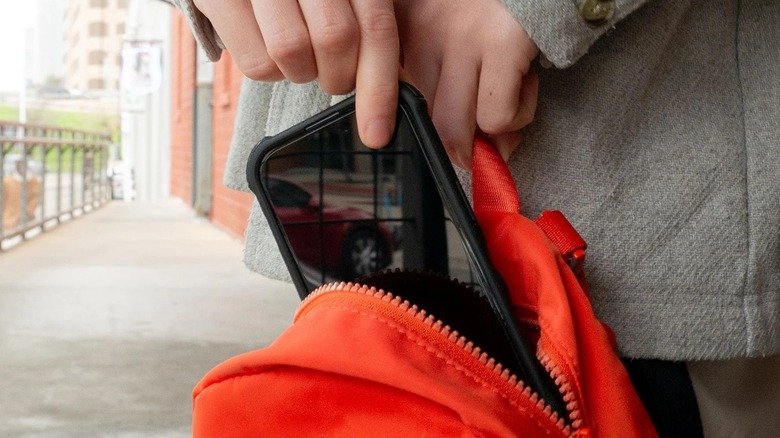 A person putting a smartphone with Smartish Tuff Sheet screen protector in a bag